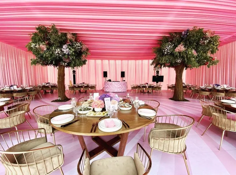 Boda en carpa rosa con árboles florales y mesas redondas